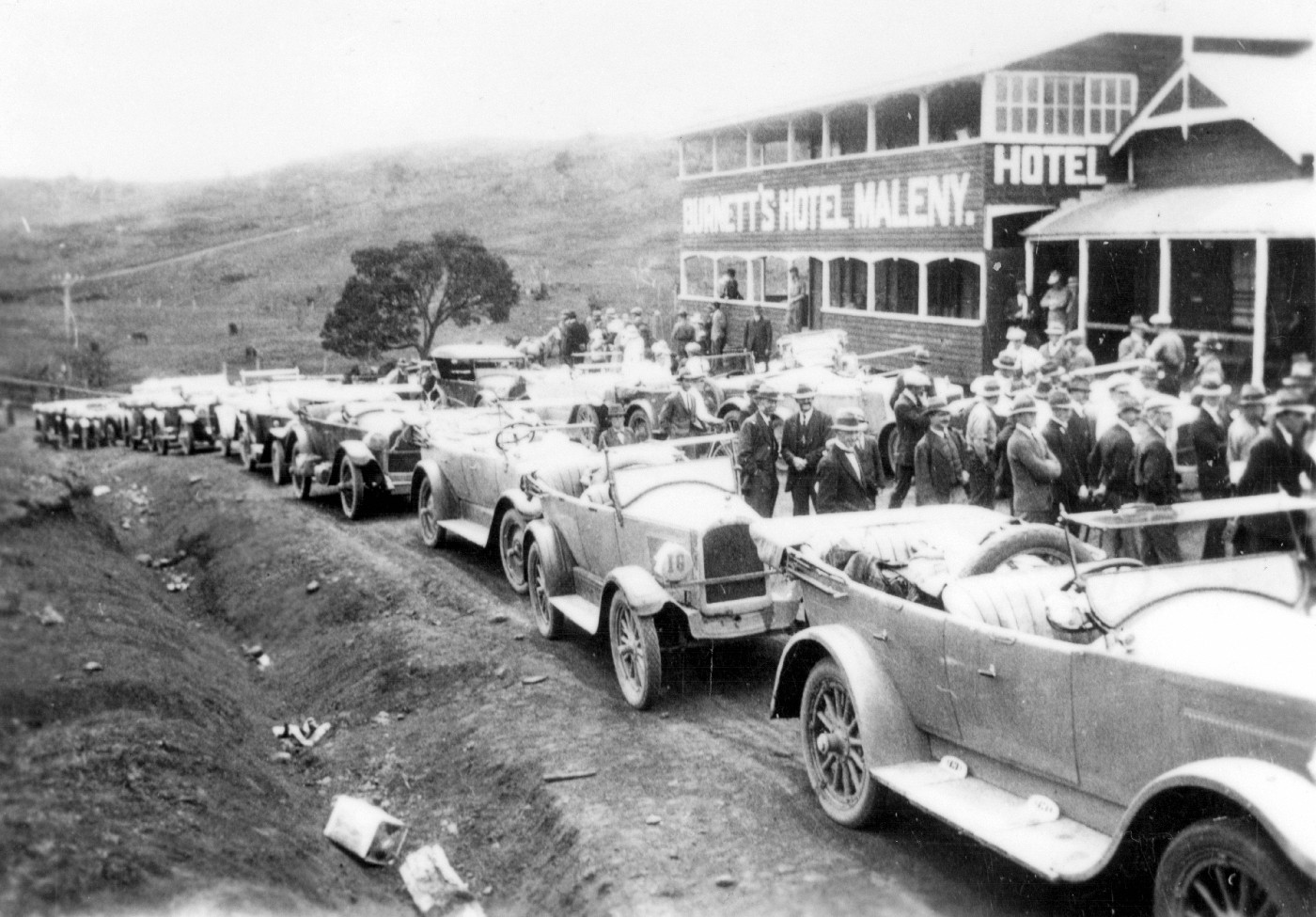 During 1921 refurbishments were made to the Hotel Maleny building and a second storey timber extension built on the Bunya Street frontage. The Burnett family owned the hotel at the time. Hotel Maleny was built by Harry Bate and Sam Sallaway in 1907, for Joseph Alfred Pollock, the first licensee, using locally pit sawn Beech timber. Model T Ford owners car rally (note numbers on headlights) are pictured gathered in Bunya Street outside the hotel. Note fuel tins cast aside in the gutters. The road leading to North Maleny can be seen in the background.